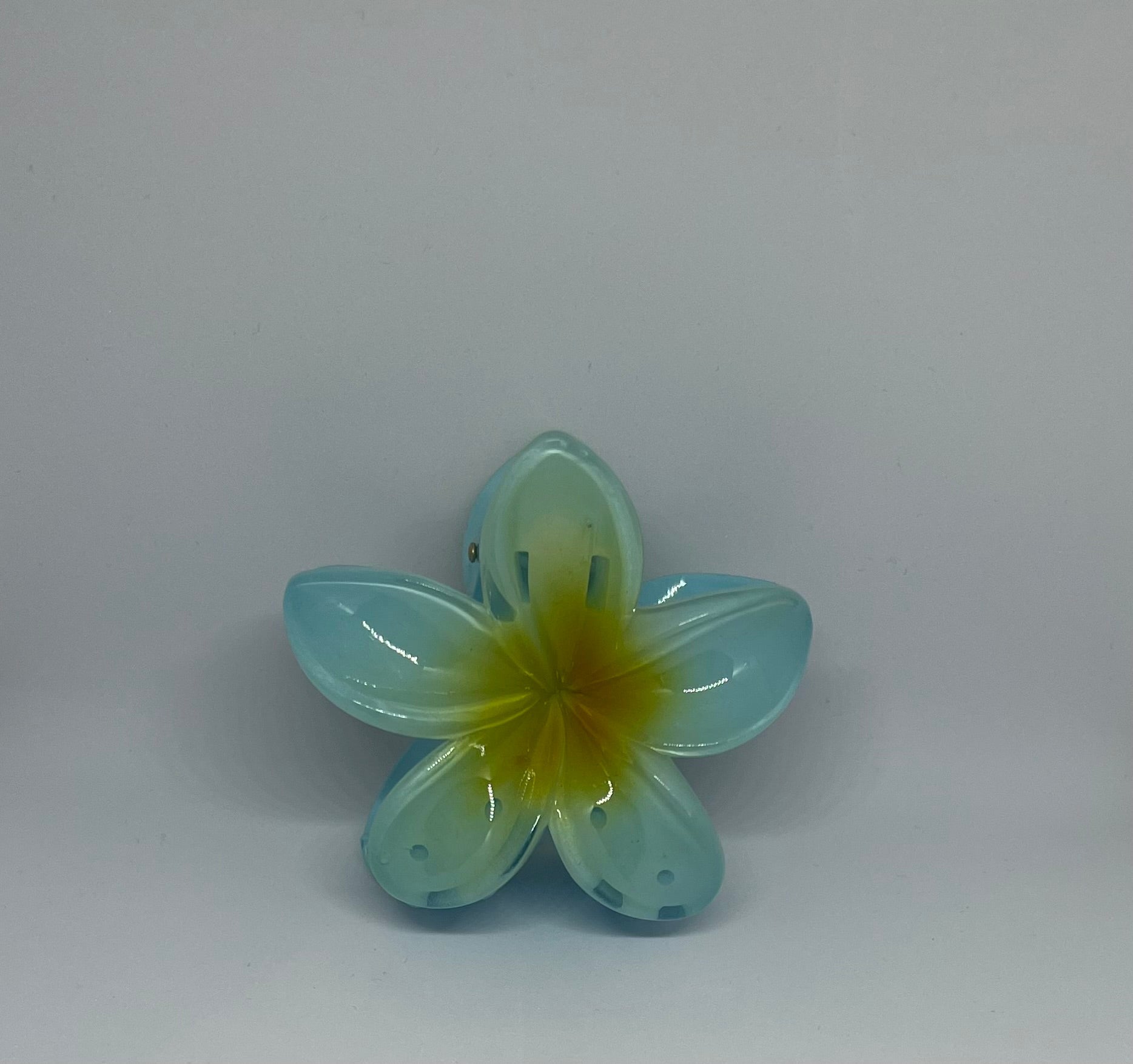 Blue frangipani flower hair claw clip with translucent sky blue petals and golden yellow centre