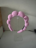 Pink terry-cloth bubble headband displayed on a clear acrylic headband stand