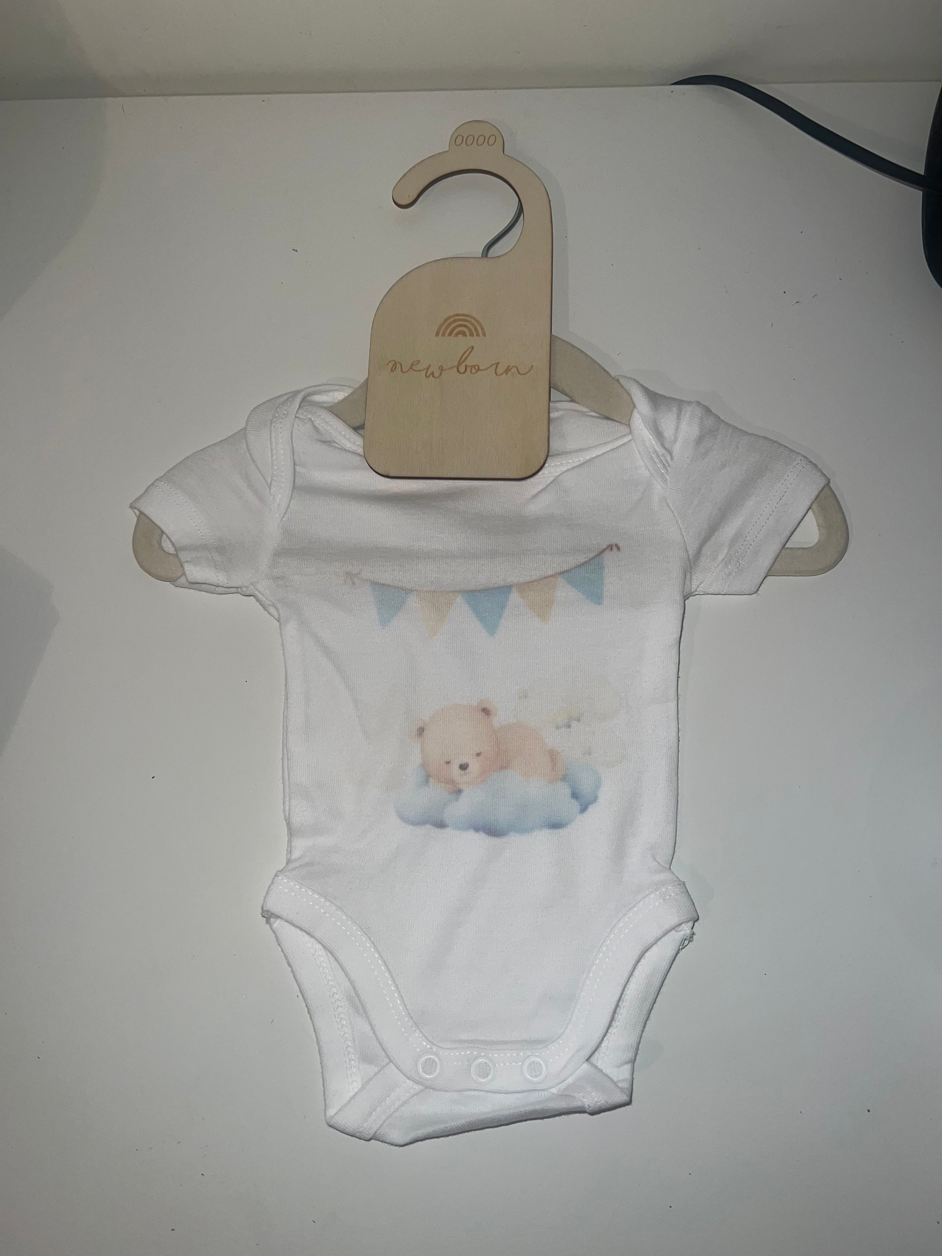 White short sleeve baby onesie with watercolour sleepy teddy bear on cloud and blue bunting print on newborn hanger