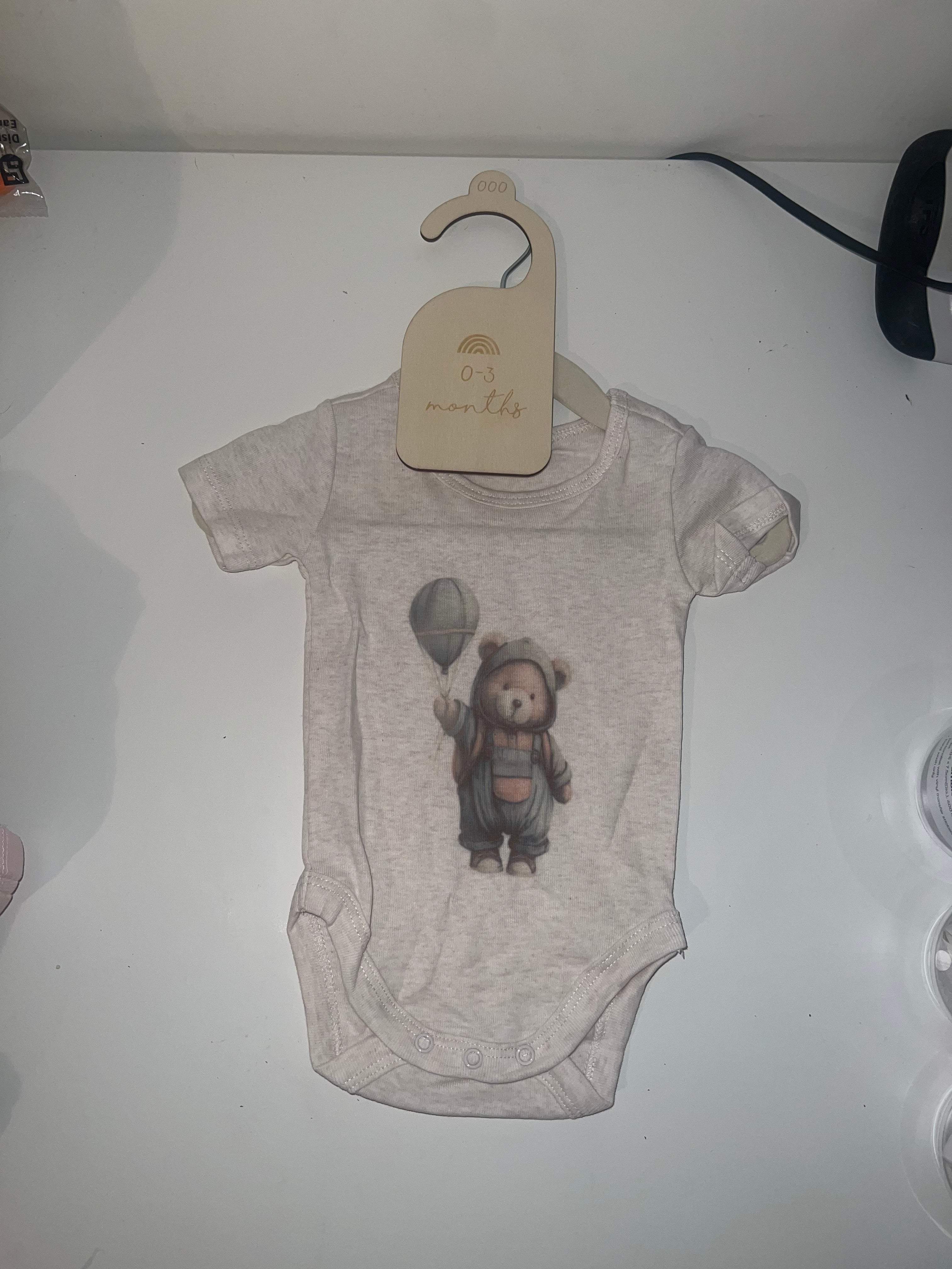 Oatmeal marle short sleeve baby onesie with bear in raincoat holding balloon illustration on 0-3 months hanger