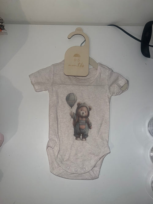 Oatmeal marle short sleeve baby onesie with bear in raincoat holding balloon illustration on 0-3 months hanger