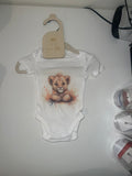 White short sleeve baby onesie with watercolour lion cub illustration in warm golden tones on 0-3 months hanger