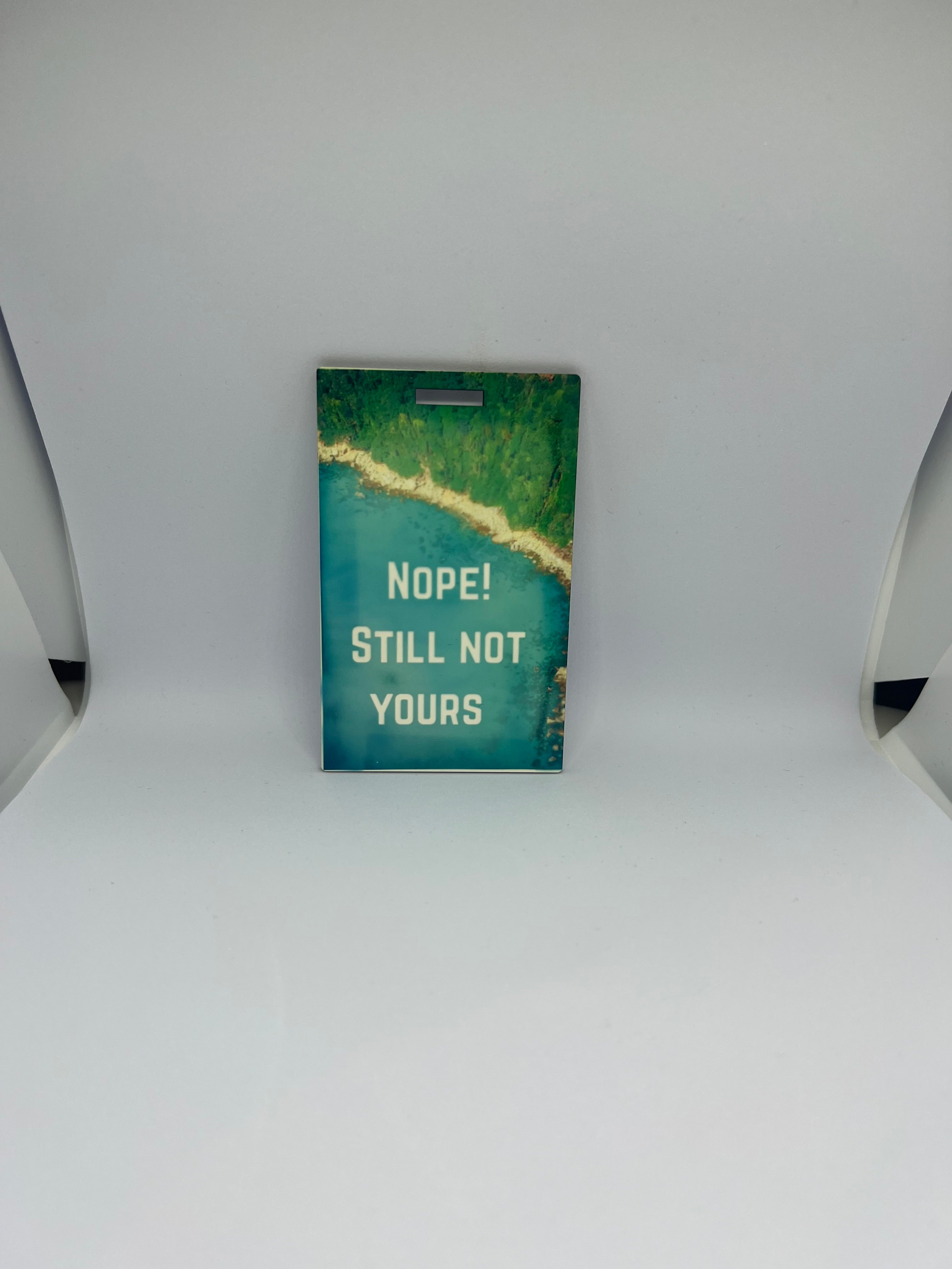Nope Still Not Yours luggage tag with bold white text over aerial coastal forest and turquoise water