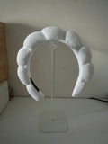 White terry-cloth bubble headband displayed on a clear acrylic headband stand